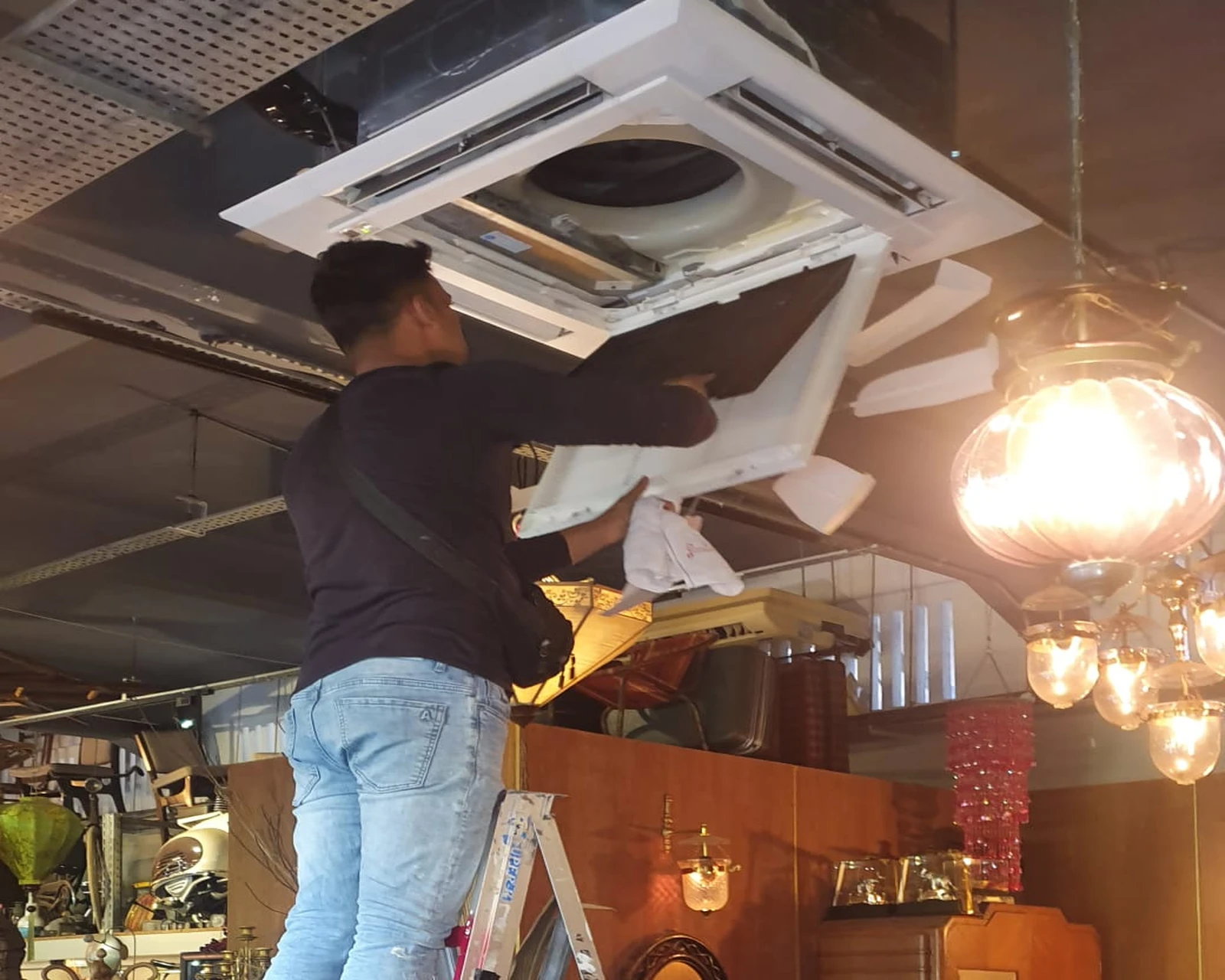Technician performing indoor aircon servicing on a ceiling cassette unit